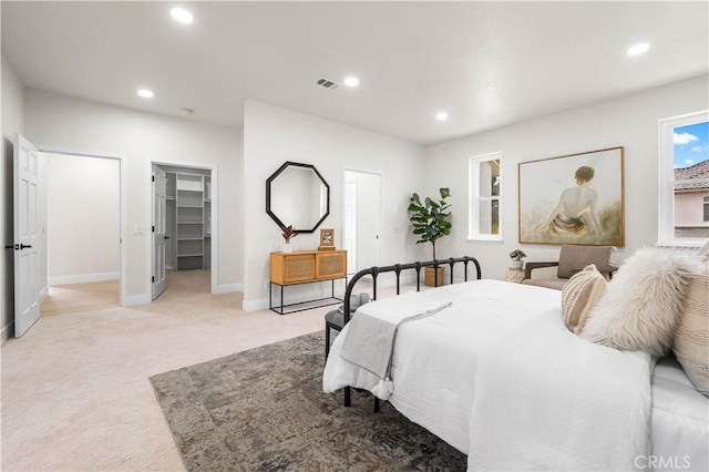 bedroom featuring recessed lighting, light carpet, visible vents, baseboards, and a walk in closet