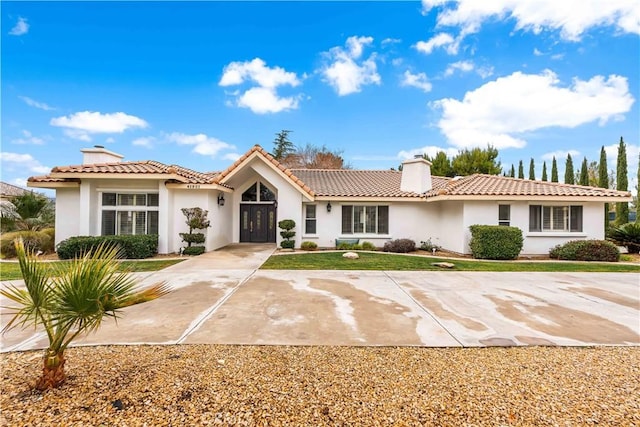 view of front facade featuring a tile roof, concrete driveway, stucco siding, a chimney, and a front yard