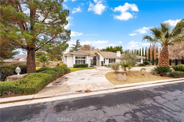 view of front of house featuring concrete driveway, a tile roof, a chimney, and stucco siding