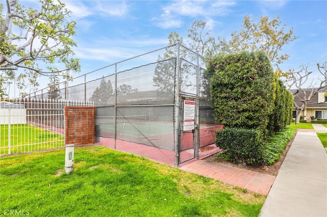 view of tennis court with a gate, a yard, and fence