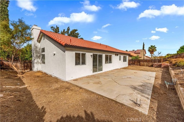 rear view of house featuring a tile roof, a chimney, stucco siding, a patio area, and a fenced backyard