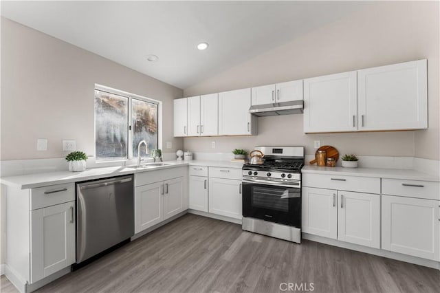 kitchen featuring stainless steel appliances, white cabinetry, vaulted ceiling, a sink, and under cabinet range hood