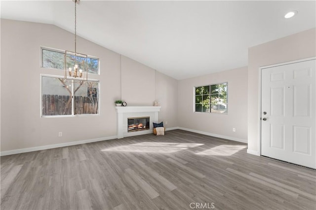 unfurnished living room featuring baseboards, a glass covered fireplace, wood finished floors, an inviting chandelier, and vaulted ceiling