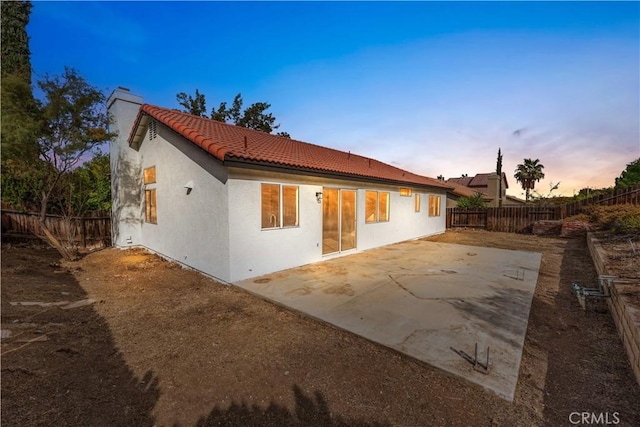 rear view of property with a patio, a fenced backyard, a tile roof, stucco siding, and a chimney