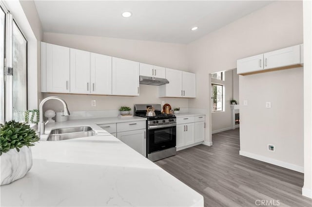 kitchen with stainless steel gas stove, white cabinets, vaulted ceiling, under cabinet range hood, and a sink