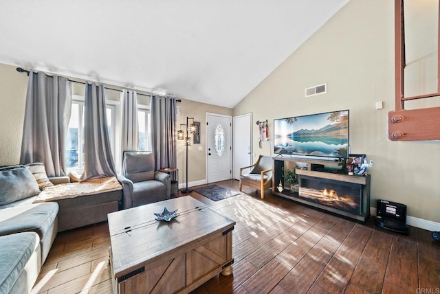 living area with visible vents, a glass covered fireplace, wood finished floors, high vaulted ceiling, and baseboards