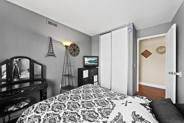 bedroom with a closet, wood finished floors, visible vents, and baseboards