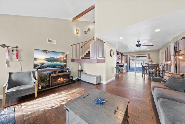 living area featuring a warm lit fireplace, baseboards, visible vents, and wood finished floors