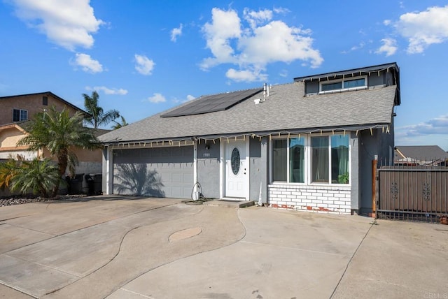 view of front of home with concrete driveway, a shingled roof, solar panels, and brick siding