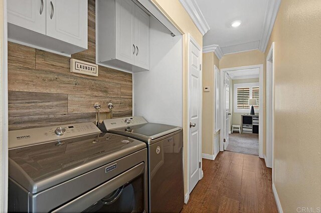 laundry room featuring cabinet space, baseboards, dark wood-style floors, crown molding, and washing machine and dryer