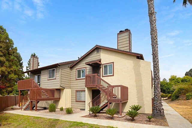 rear view of house featuring stairway, a chimney, fence, and stucco siding