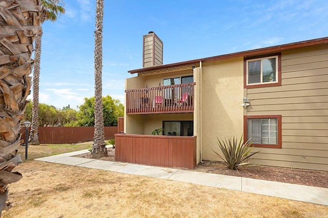 rear view of property featuring a chimney, fence, a balcony, and stucco siding