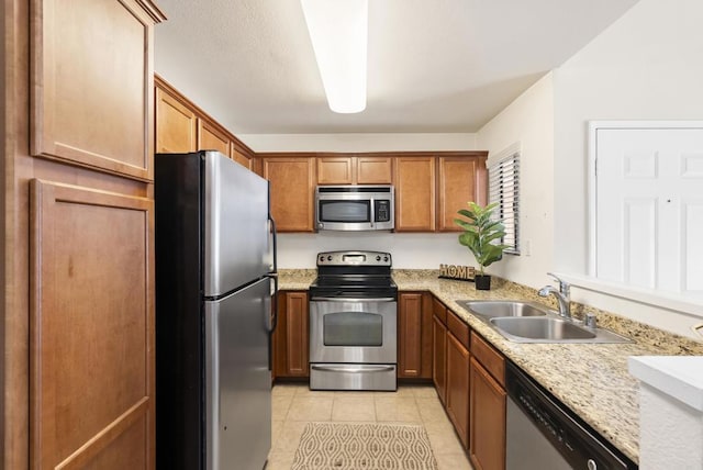 kitchen with light tile patterned floors, appliances with stainless steel finishes, a sink, and brown cabinets