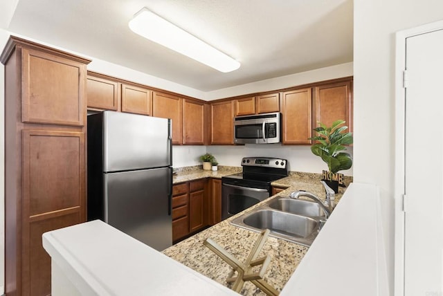 kitchen featuring brown cabinetry, stainless steel appliances, a sink, and light countertops