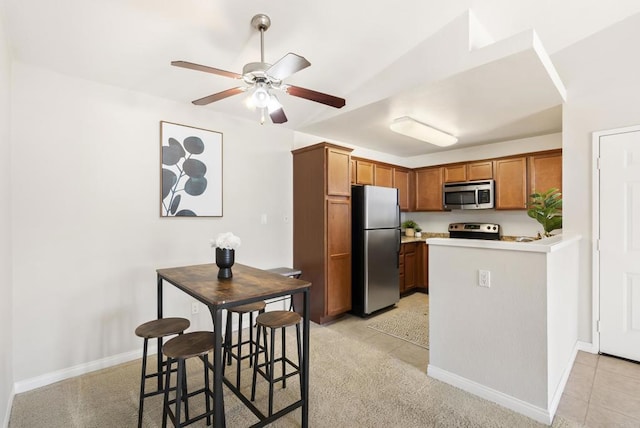 kitchen with a peninsula, baseboards, light countertops, appliances with stainless steel finishes, and brown cabinetry