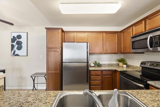 kitchen featuring light stone counters, appliances with stainless steel finishes, brown cabinetry, and a sink