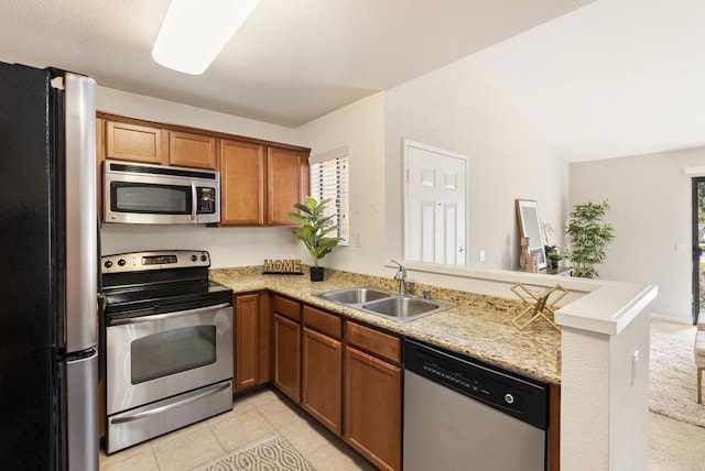 kitchen with brown cabinets, stainless steel appliances, light tile patterned flooring, a sink, and a peninsula