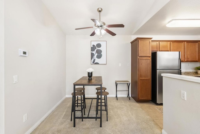 kitchen with baseboards, brown cabinetry, freestanding refrigerator, and light colored carpet