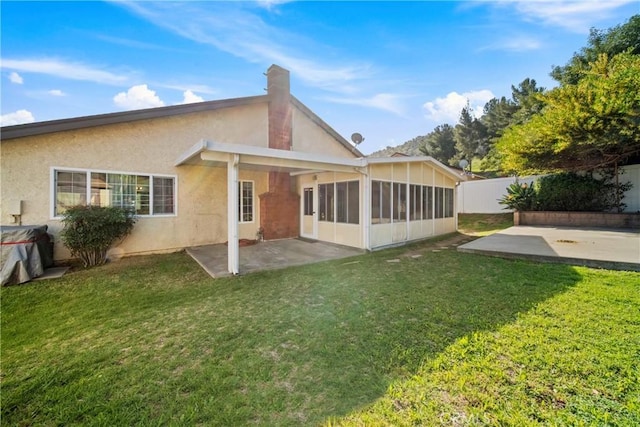 back of house featuring a lawn, a sunroom, fence, a patio area, and stucco siding