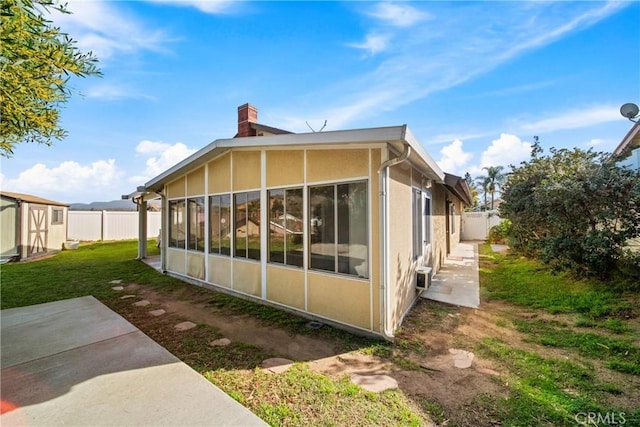 rear view of house with a sunroom, a fenced backyard, a chimney, and an outdoor structure