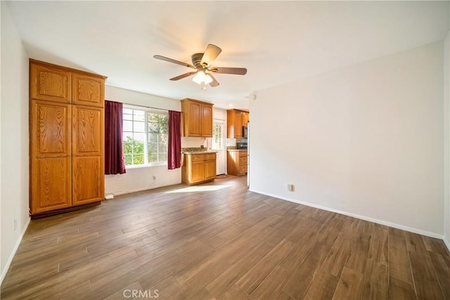 unfurnished living room with ceiling fan, dark wood-style flooring, and baseboards