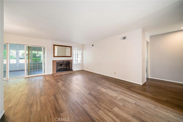 unfurnished living room featuring a brick fireplace, visible vents, baseboards, and wood finished floors