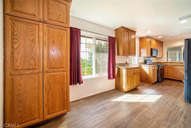 kitchen with recessed lighting, appliances with stainless steel finishes, brown cabinetry, light wood-type flooring, and baseboards