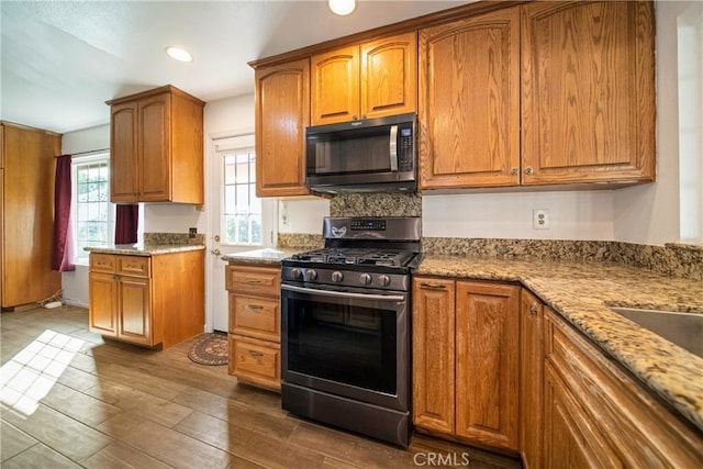 kitchen with stainless steel gas stove, light stone countertops, and brown cabinets