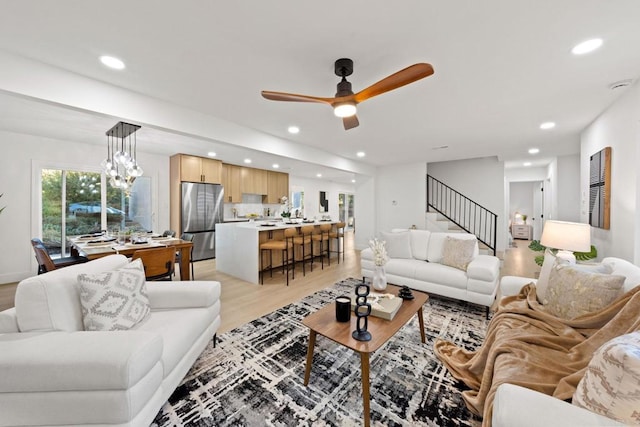 living area featuring light wood-style floors, recessed lighting, stairway, and ceiling fan with notable chandelier