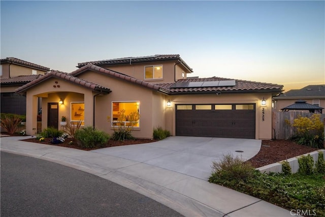 mediterranean / spanish home with concrete driveway, solar panels, a tile roof, an attached garage, and stucco siding