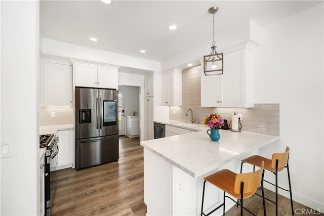 kitchen with wood finished floors, a peninsula, stainless steel appliances, white cabinetry, and a sink