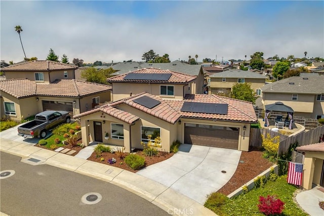 mediterranean / spanish-style home featuring stucco siding, solar panels, fence, a garage, and a residential view