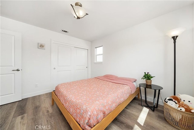 bedroom with a closet, wood finished floors, visible vents, and baseboards