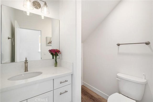 bathroom featuring toilet, wood finished floors, vanity, baseboards, and vaulted ceiling