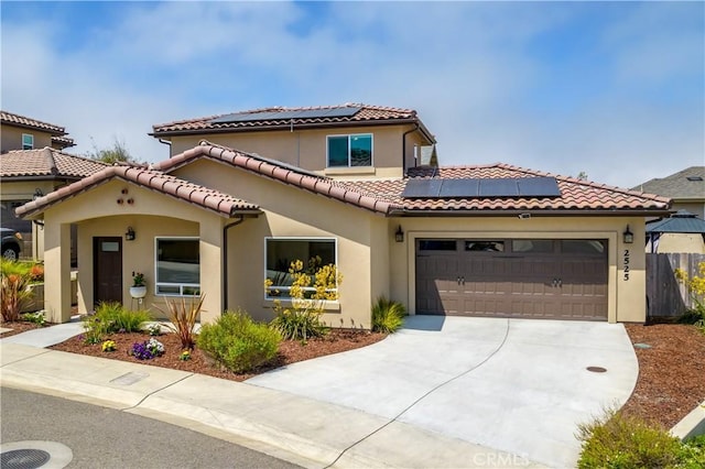 mediterranean / spanish home featuring an attached garage, driveway, roof mounted solar panels, and stucco siding