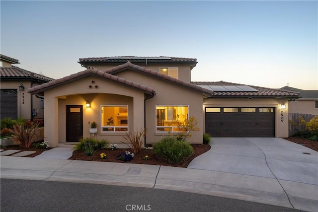 mediterranean / spanish-style house featuring a garage, roof mounted solar panels, a tile roof, and stucco siding