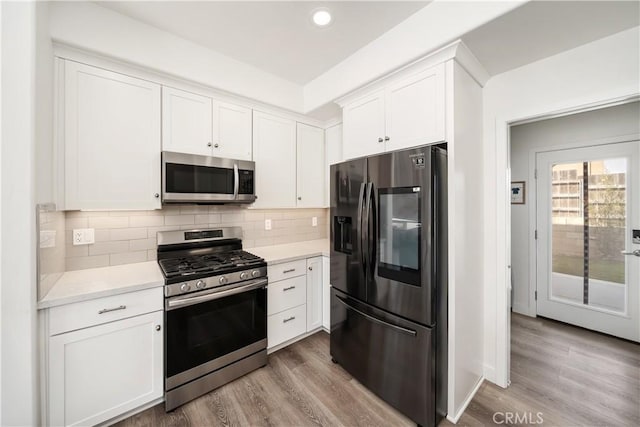 kitchen with recessed lighting, wood finished floors, white cabinetry, appliances with stainless steel finishes, and tasteful backsplash