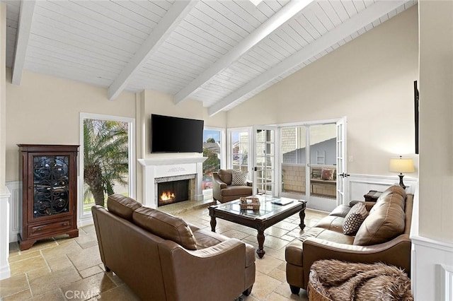 living room featuring beamed ceiling, a lit fireplace, stone tile flooring, and wooden ceiling