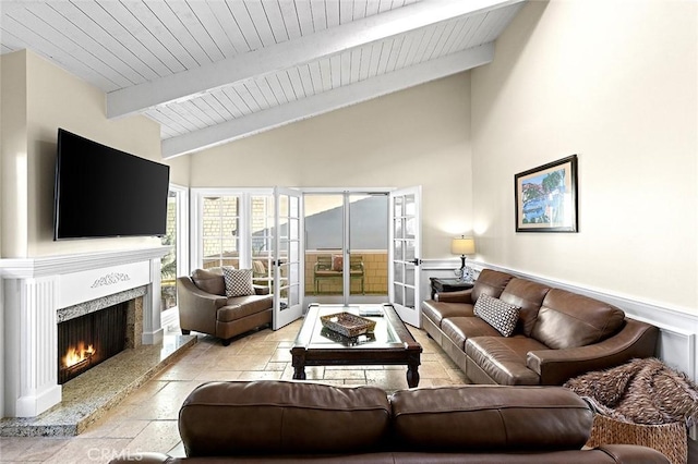 living area featuring a wainscoted wall, wood ceiling, beam ceiling, a fireplace, and stone tile flooring