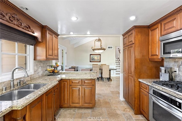 kitchen with stone tile floors, a peninsula, brown cabinetry, stainless steel appliances, and a sink