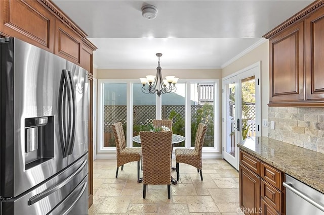 kitchen with ornamental molding, stone tile floors, stainless steel appliances, an inviting chandelier, and decorative backsplash