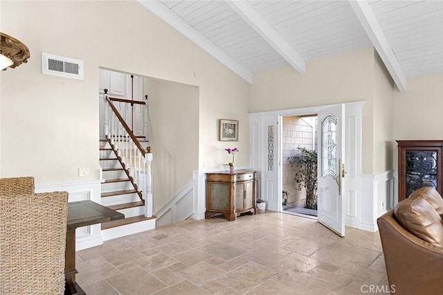 entrance foyer with visible vents, stairs, beam ceiling, stone tile flooring, and high vaulted ceiling