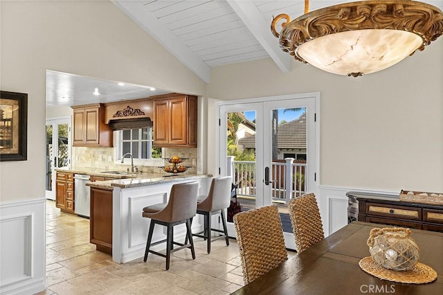 kitchen featuring a breakfast bar area, stone tile flooring, a sink, french doors, and stainless steel dishwasher