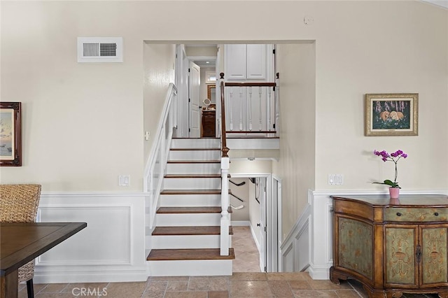 stairs featuring visible vents, a wainscoted wall, and stone finish floor