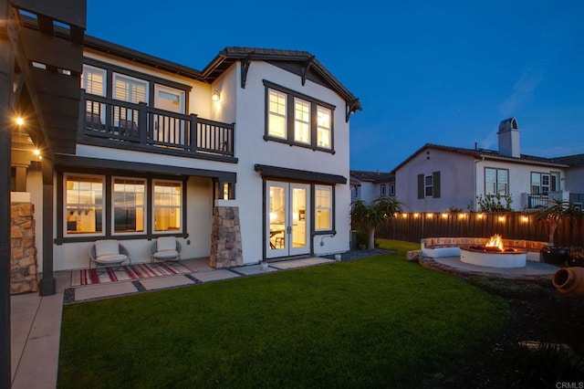 back of property with stucco siding, a lawn, french doors, a fire pit, and a balcony