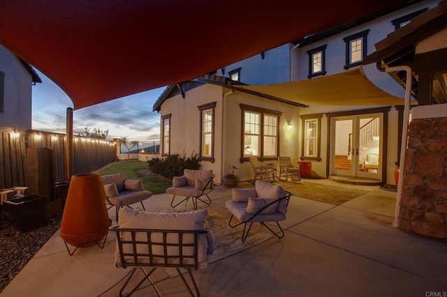 patio terrace at dusk featuring french doors, an outdoor hangout area, and fence