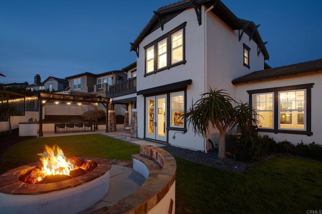 rear view of house featuring stucco siding, a patio, a balcony, and a yard