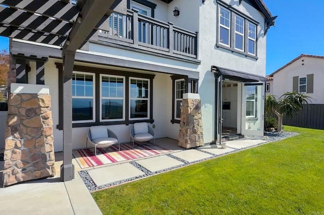 back of house with a balcony, a yard, and stucco siding