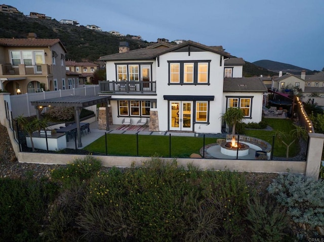 back of house with an outdoor fire pit, a lawn, a chimney, a balcony, and a patio area