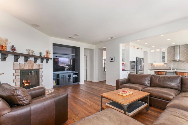 living area featuring dark wood finished floors, visible vents, a stone fireplace, and baseboards